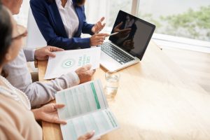 Senior couple studying terms of life insurance policy while having meeting with highly professional agent, interior of modern office with panoramic windows on background